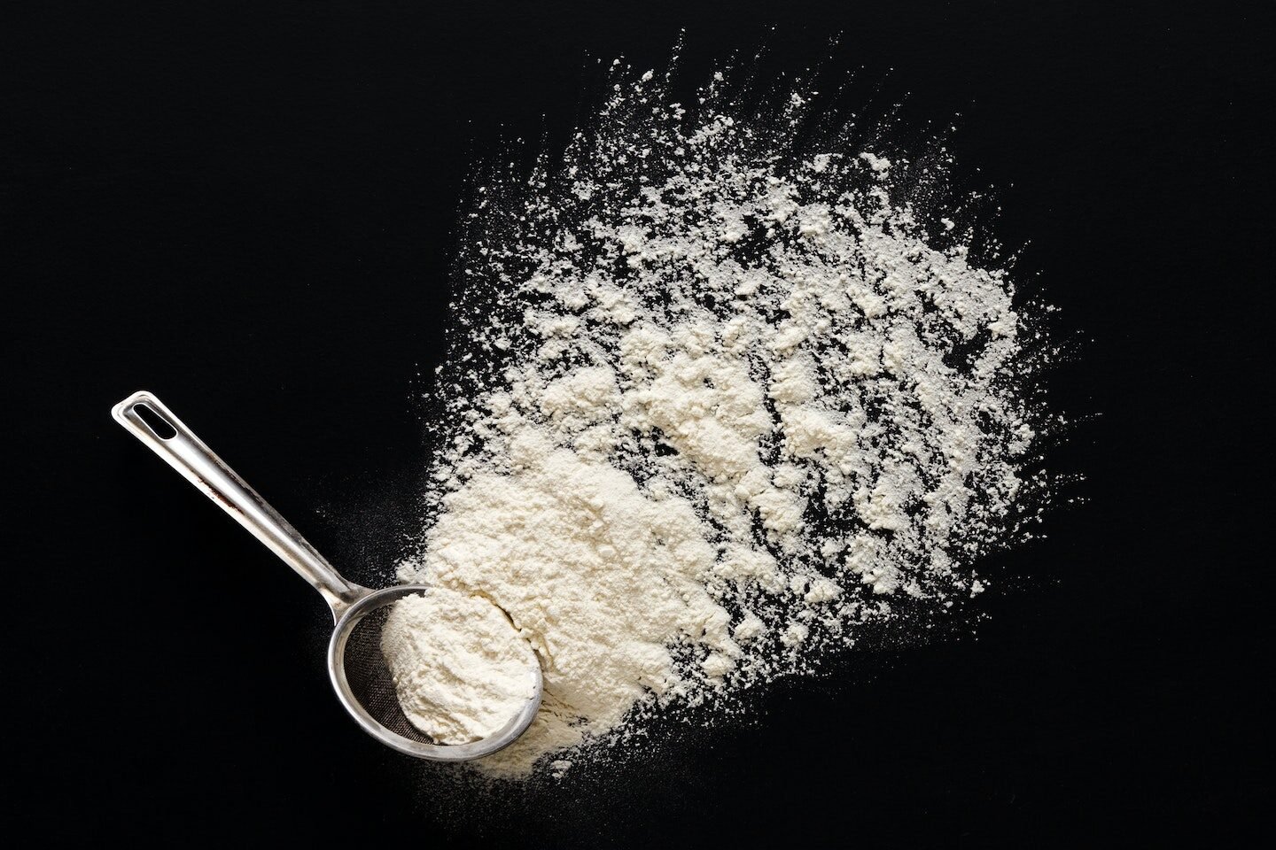 Flour on black background in measuring spoon